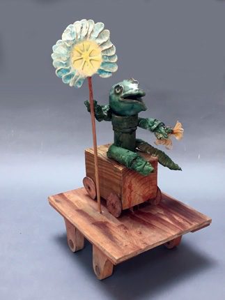 A sculpture of a frog sitting on a wooden box.