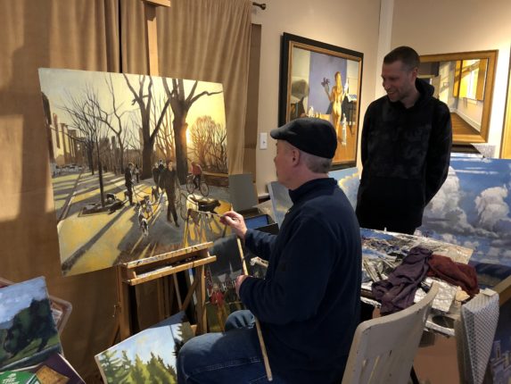 Two men sitting in front of a painting easel.