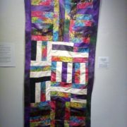 A colorful quilt hanging on a wall.