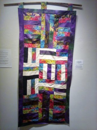 A colorful quilt hanging on a wall.