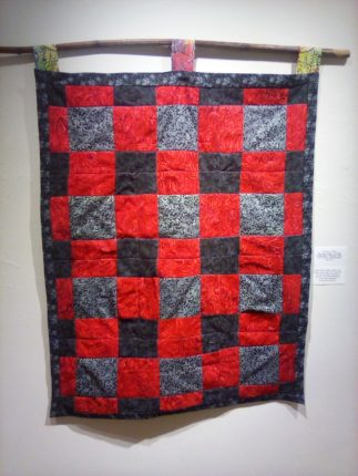 A red and black quilt hanging on a wall.