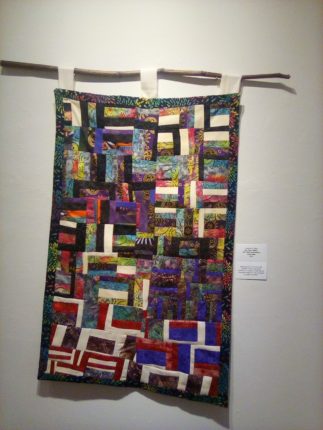 A colorful quilt hanging on a wall.