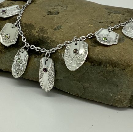 A silver necklace with several charms on top of a rock.