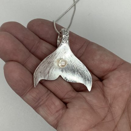 A hand holding a silver mermaid tail pendant.