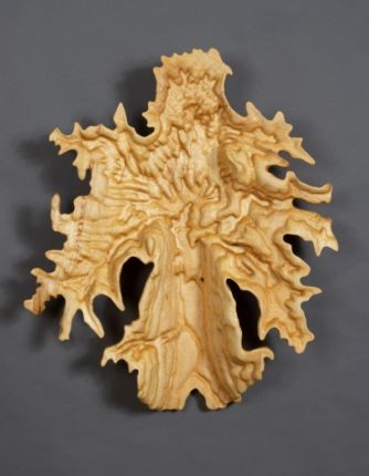 A wood carving of a leaf on a gray background.