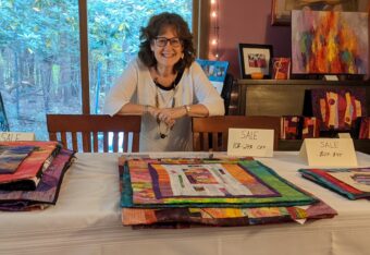 A woman standing in front of a table full of quilts.