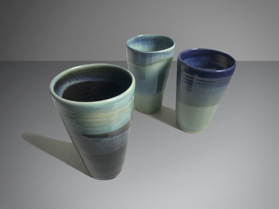 Three blue and green vases on a grey surface.