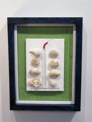 A framed piece of art with shells and a candle.
