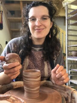 A woman in glasses is holding a cup in a pottery studio.