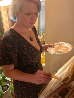 A woman holding a plate of paint in front of an easel.