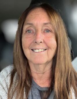 An older woman smiling in the back seat of a car.