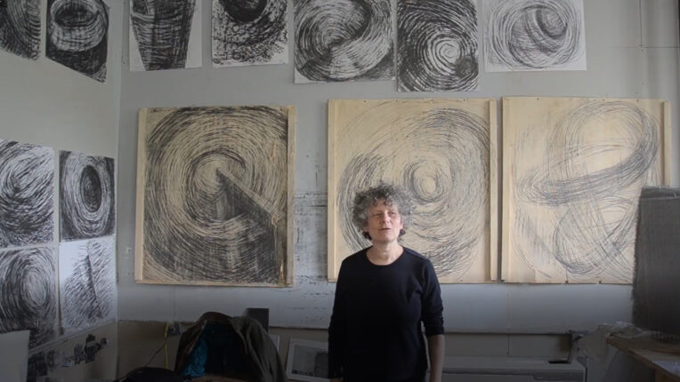 A woman standing in front of some drawings.