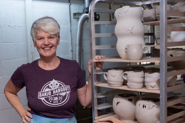 A woman standing in front of a rack of mugs.