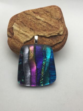 A colorful glass pendant sitting on top of a rock.