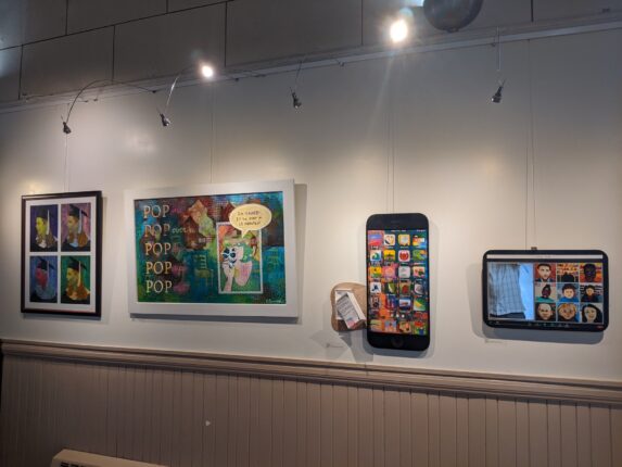 A wall with several different pictures and a cell phone.