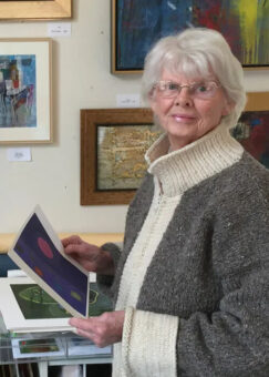 An older woman holding up a piece of art.