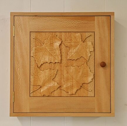 A wooden box with a carved maple leaf design.