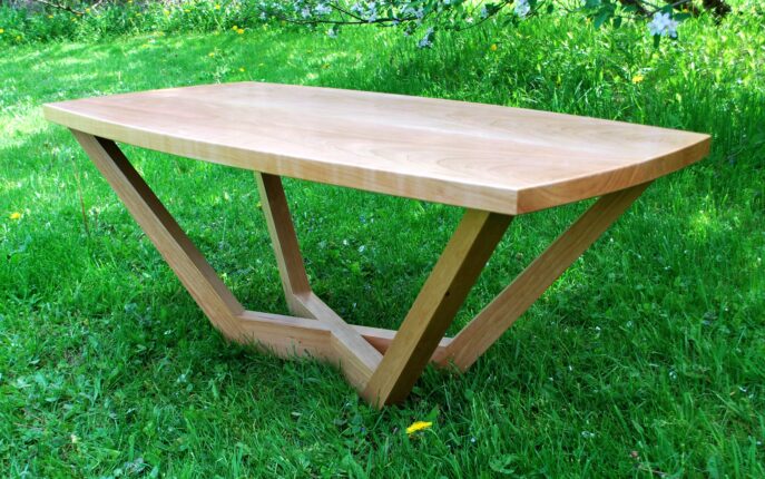 A wooden table sitting in the grass near some bushes.