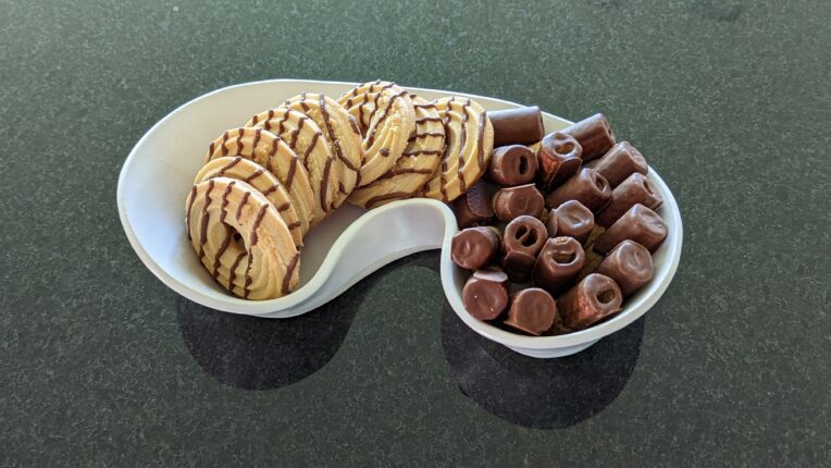A white bowl with chocolates and cookies in it.